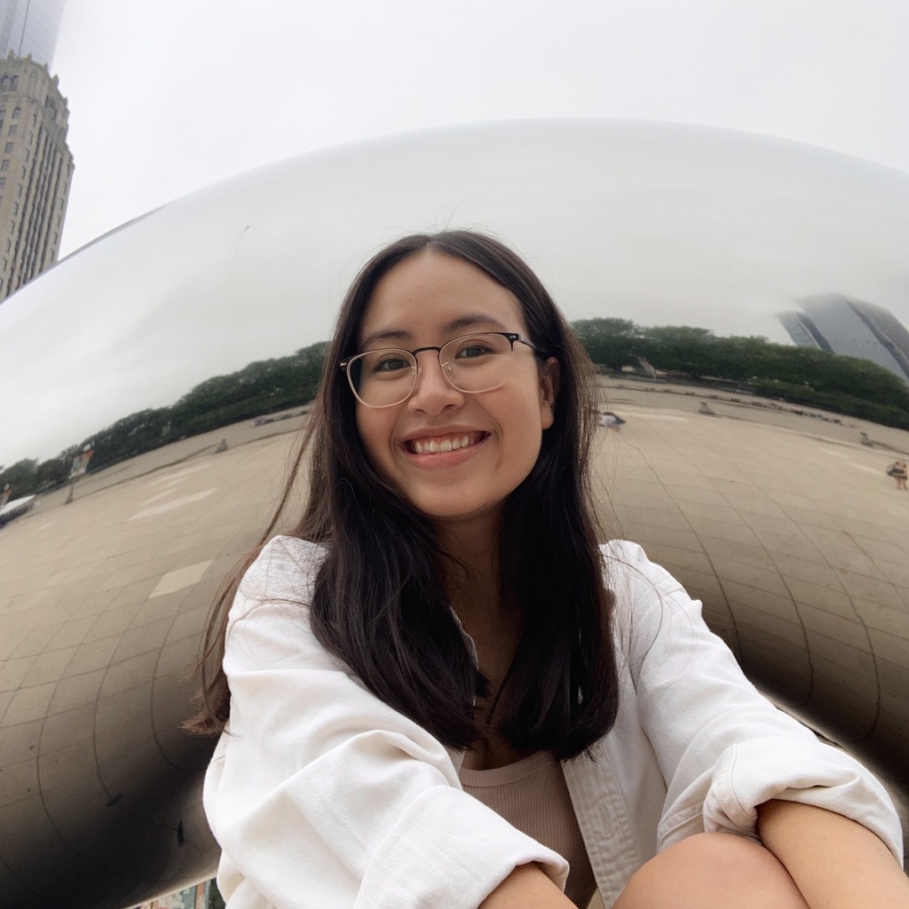 Michelle is sitting in front of the Chicago Bean, smiling into the camera.