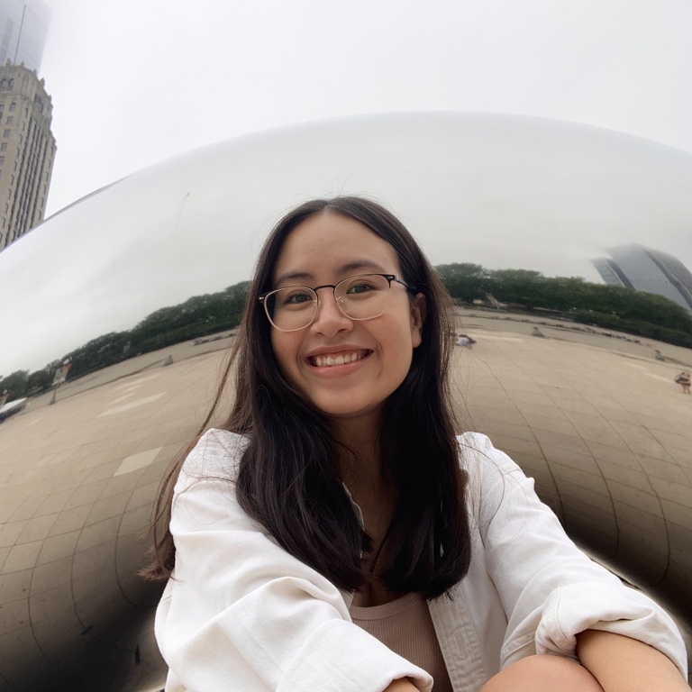 Michelle is sitting in front of the Chicago Bean, smiling into the camera.