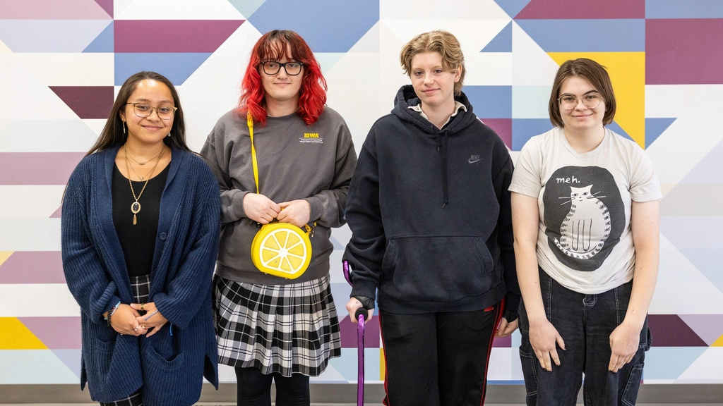 Four Pride Alliance Center student staff smiling at the camera, posing in front of a geometric background