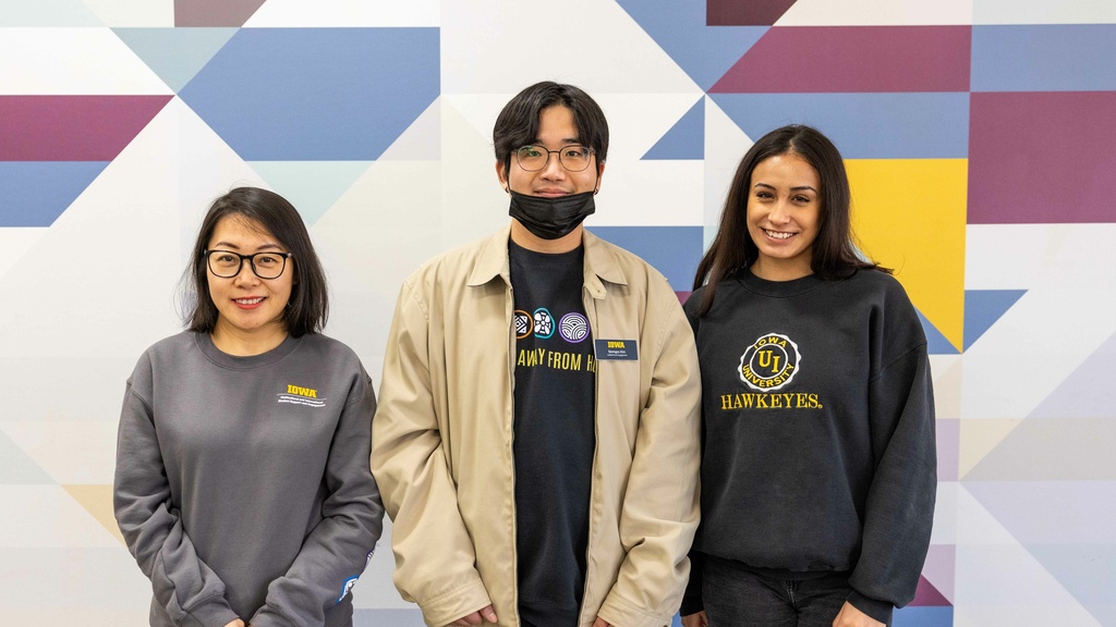 Three ISSE student staff members smiling into the camera, posing in front of a geometric background