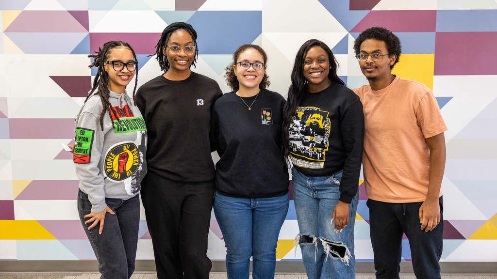 5 Afro-American Cultural center student staff smiling at the camera, posing in front of a geometric wall